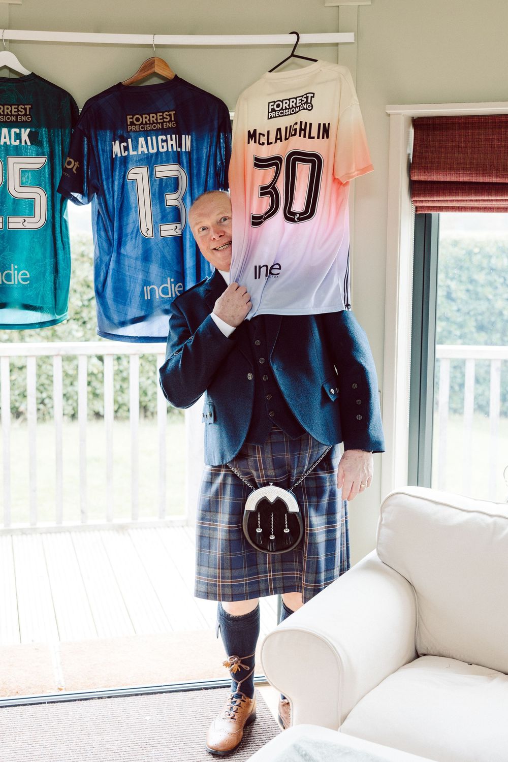 Sports jerseys and uniforms displayed on hangers against white walls in a room with natural lighting.