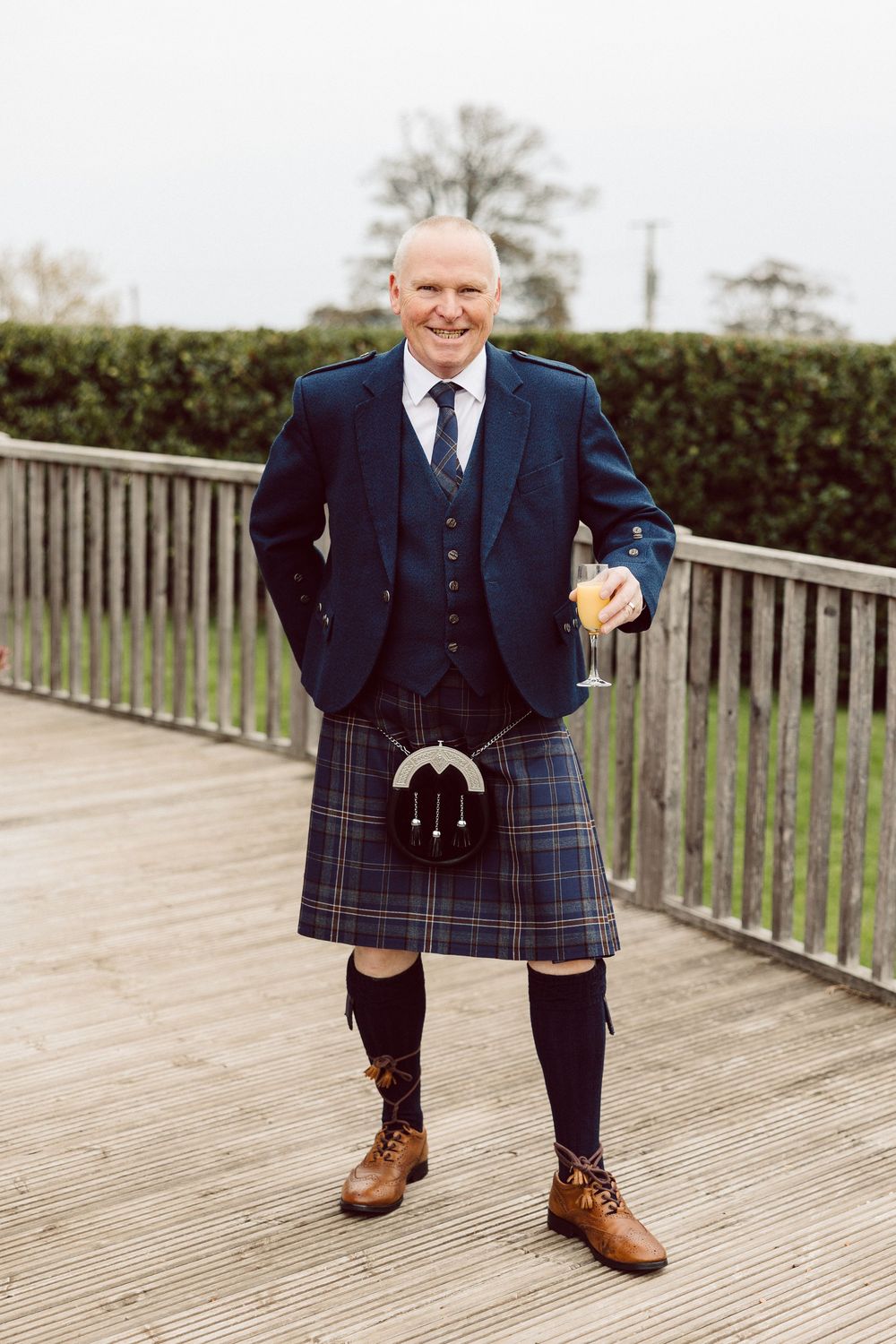 Close up shots of brown leather dress shoes paired with a traditional navy and red plaid Scottish kilt on wooden deck.
