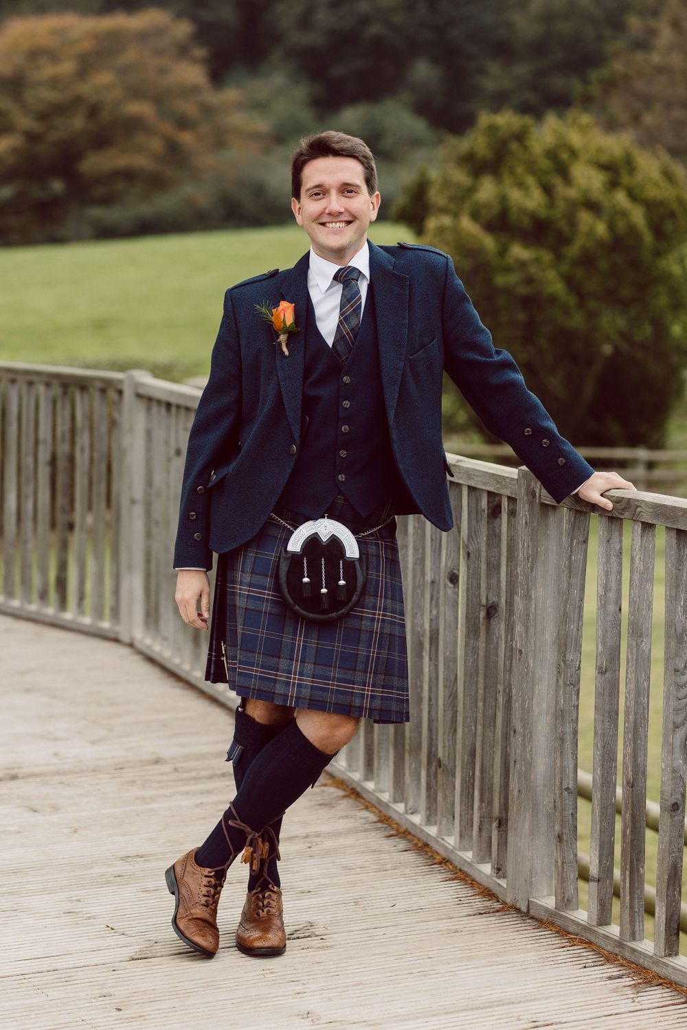 Men in Scottish formal wear striking fun poses on a wooden walkway.