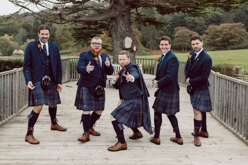 A sequence of four photos showing groomsmen in navy suits and brown boots posing on a wooden bridge.