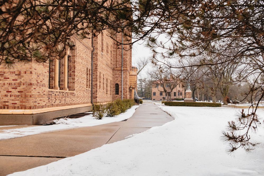 A snowy winter path leads through a historic stone building complex on a college campus.
