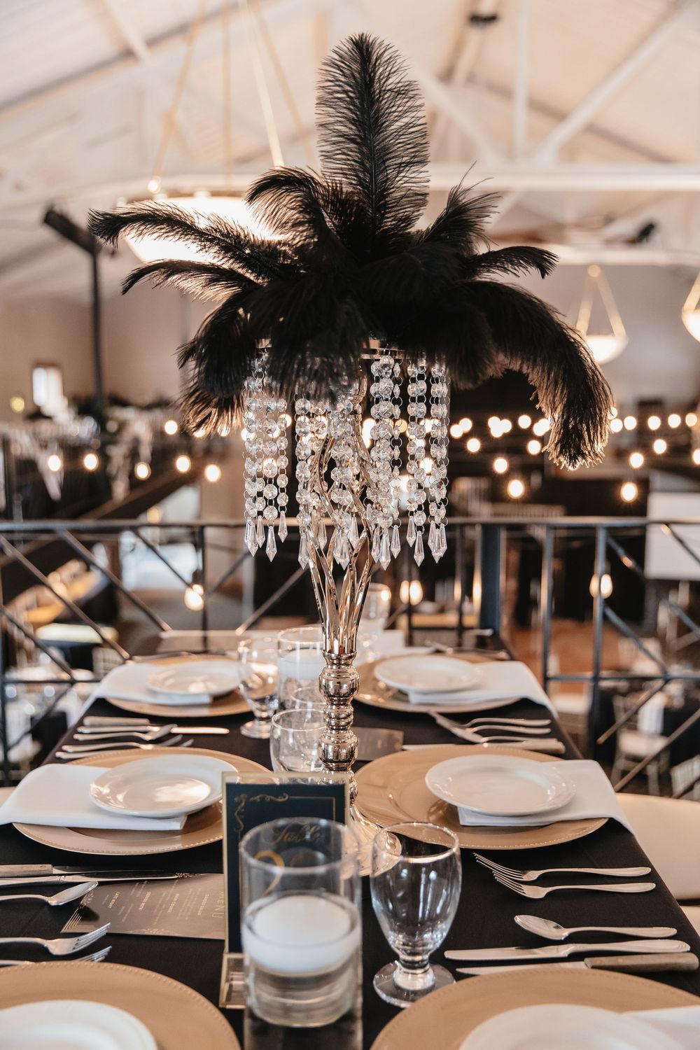 Elegant table settings with black feather centerpieces and crystal chandeliers at formal event.