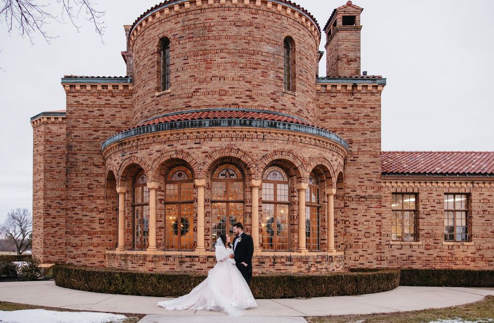 Wedding couple poses in front of ornate circular stone church with Romanesque architecture.