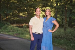 Husband and wife in coordinating outfits posing with joyous smiles on their Joppa MD driveway for L Buchanan Photography