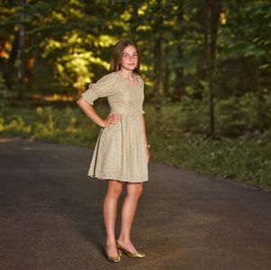 14-year-old girl in sage green dress posing on her family's asphalt driveway for a family photo session outside Baltimore