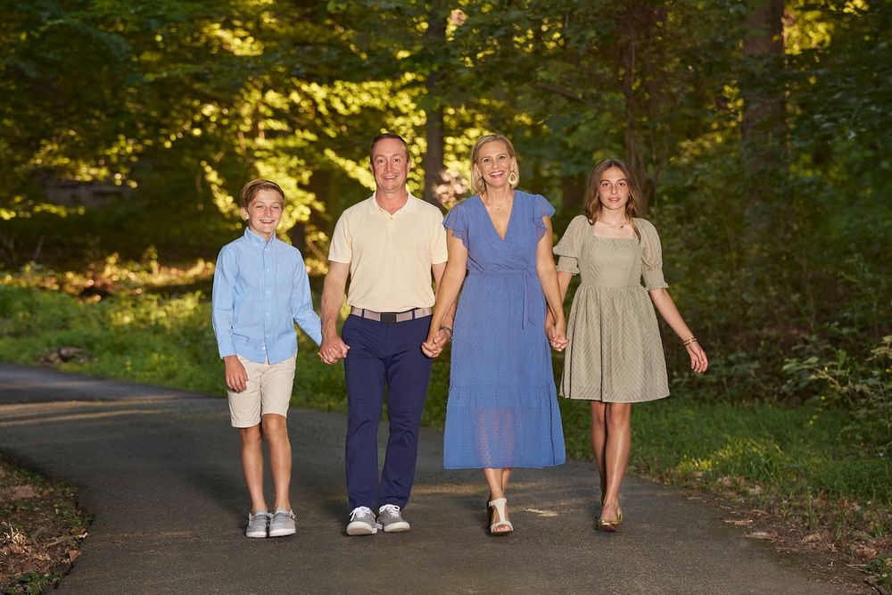 A family of four walking hand-in-hand toward L Buchanan Photography on their wooded driveway