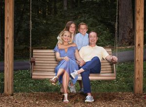 Parents on wood swing with teen son and daughter embracing them from behind during photo session with L Buchanan Photography