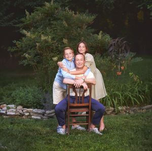 A dad and two tween and teen children happily hugging in an outdoor backyard scene outside the Baltimore Metro area