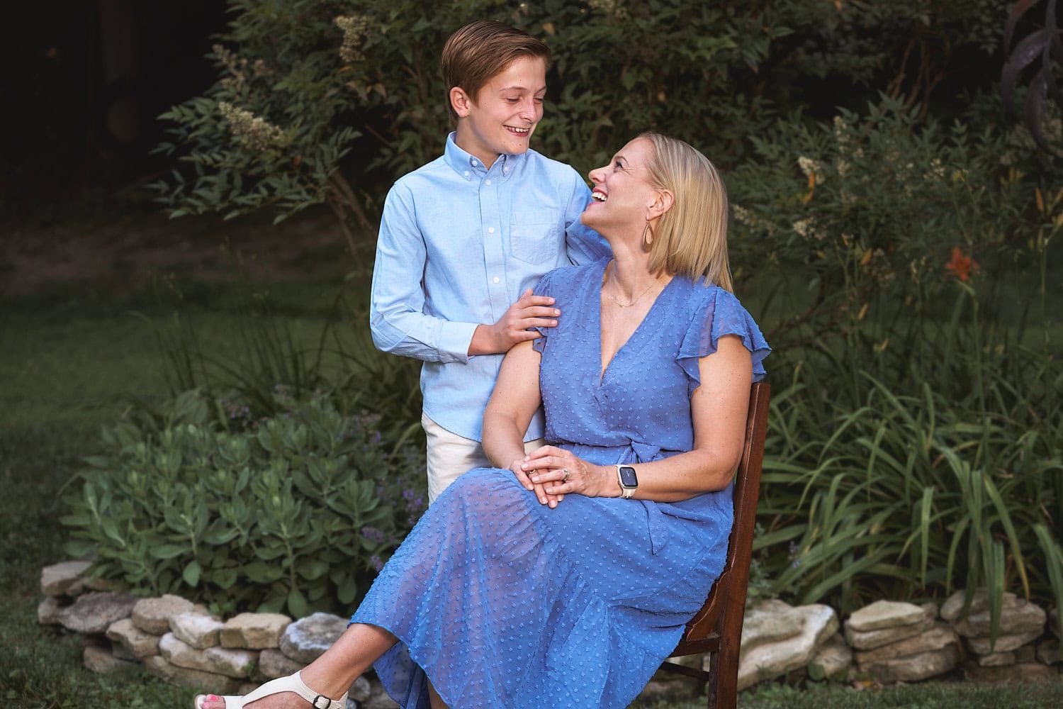 Seated mom and tween son gazing down at her in coordinating blue colors in their Baltimore outskirts  garden.