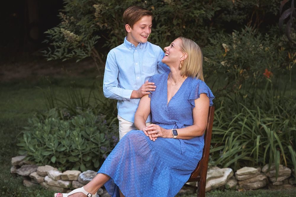 Seated mom and tween son gazing down at her in coordinating blue colors in their Baltimore outskirts  garden.