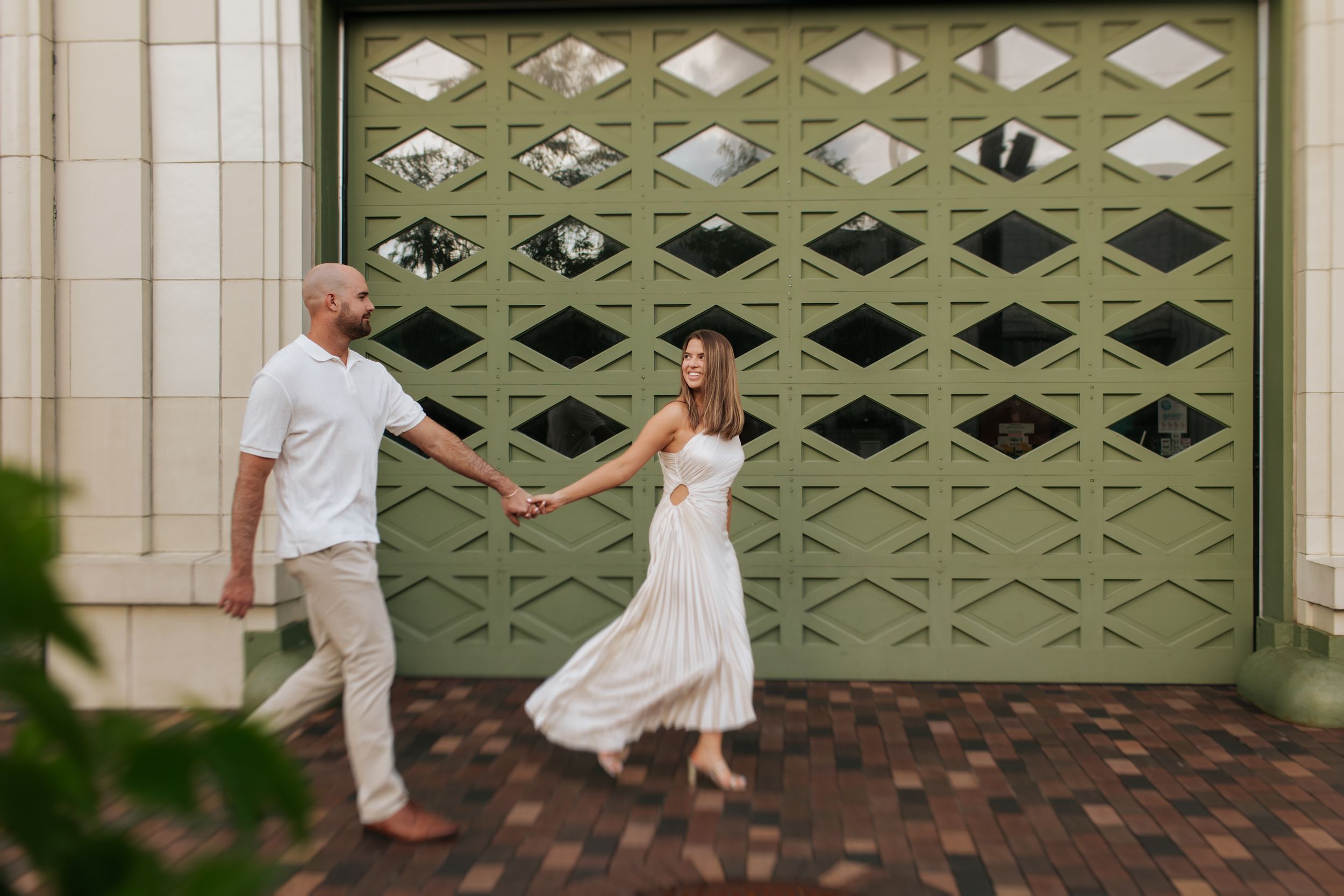 Couple dancing playfully in front of a decorative green metal gate.