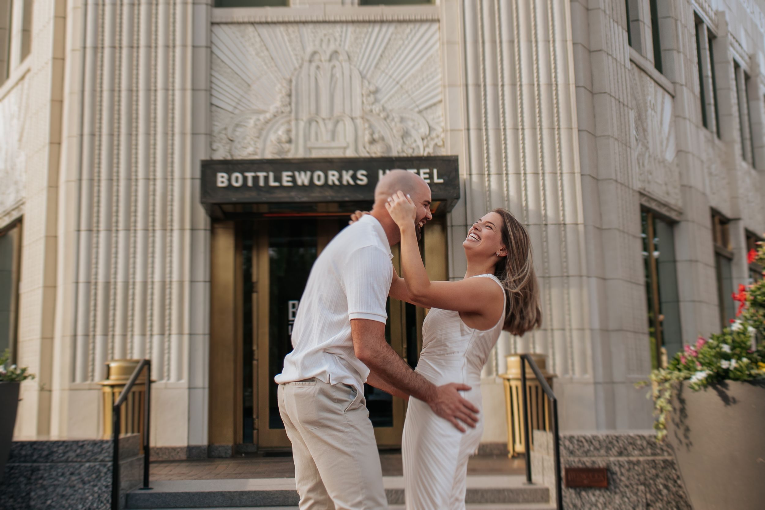 A couple dances and embraces on a city sidewalk near a storefront with classical architecture.