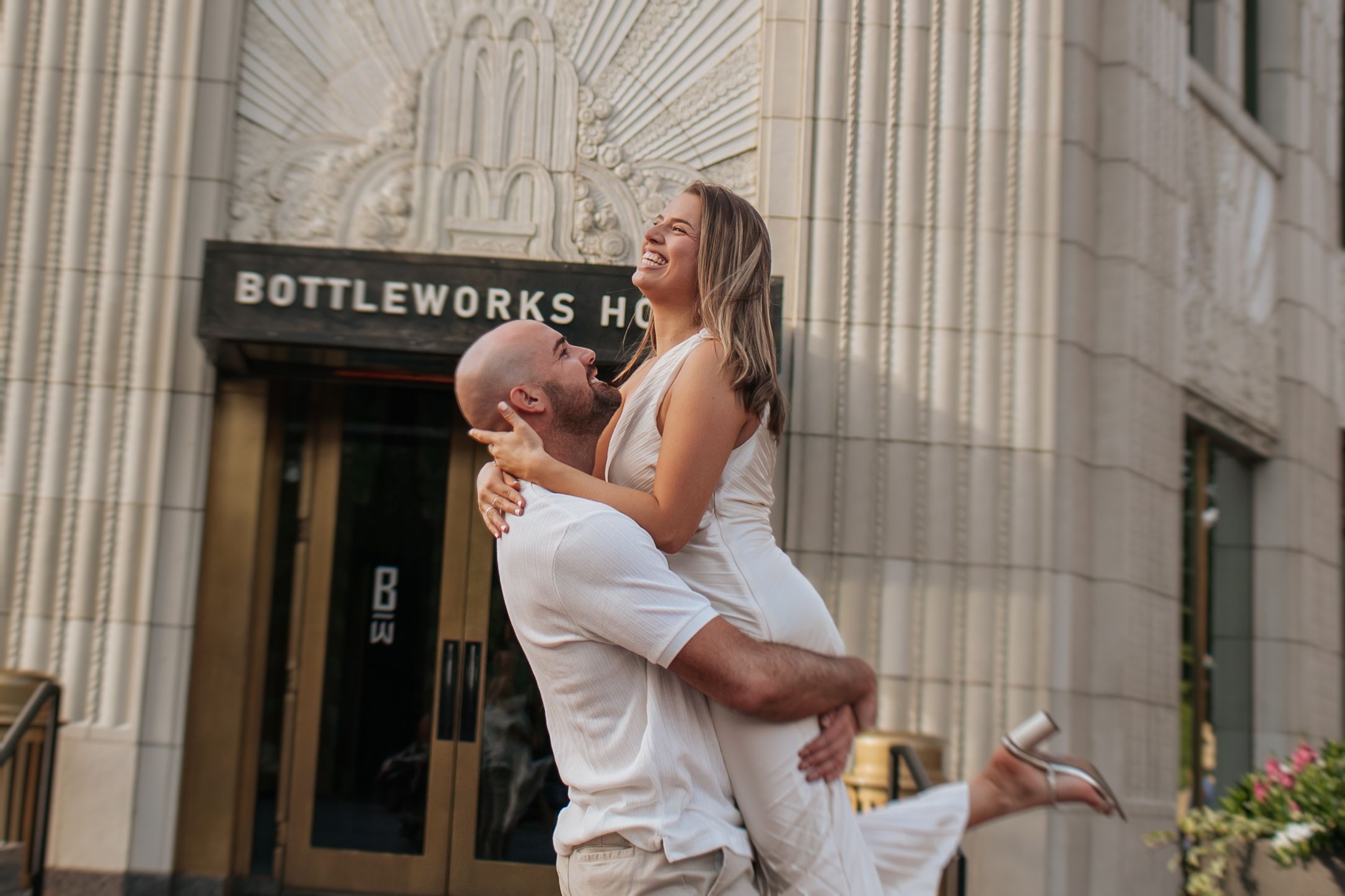 Wedding couple embraces and kisses in front of historic stone building with ornate architectural details.