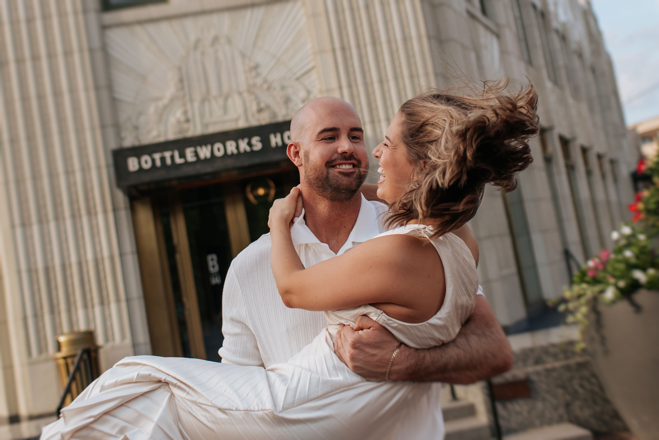 A joyful couple dances and laughs together outside a historic building with stone columns.