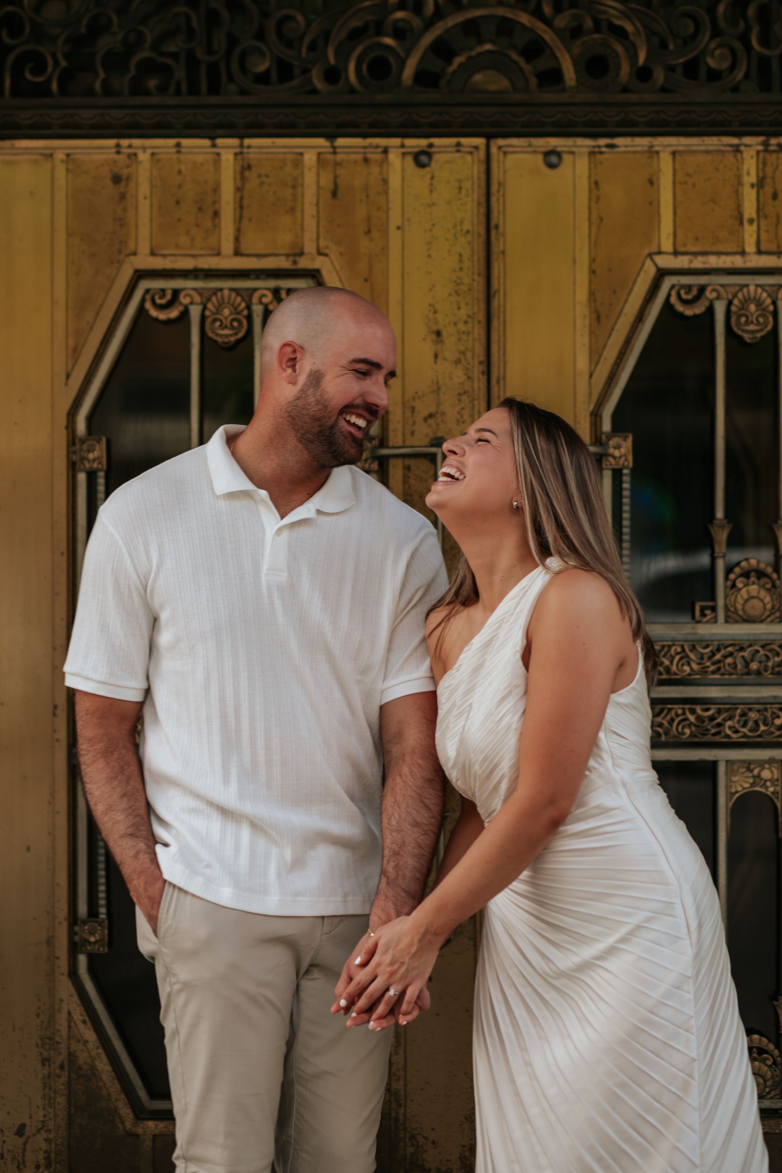 A couple in white outfits shares intimate moments and laughter against an ornate golden wall backdrop.