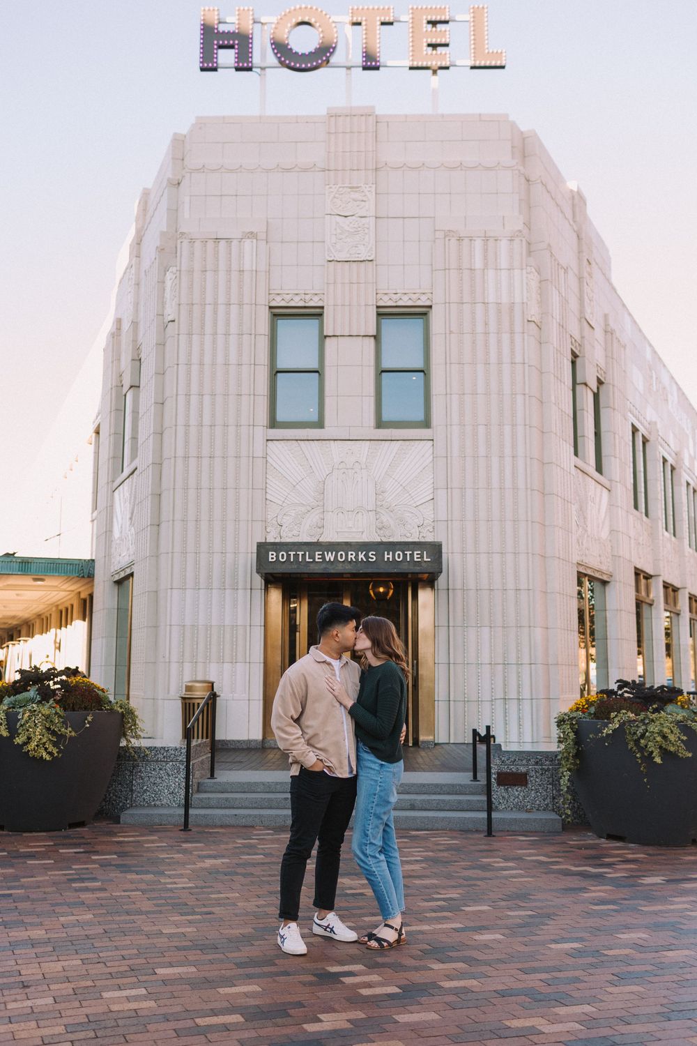 Couple sharing an intimate moment outside an Art Deco hotel building entrance.