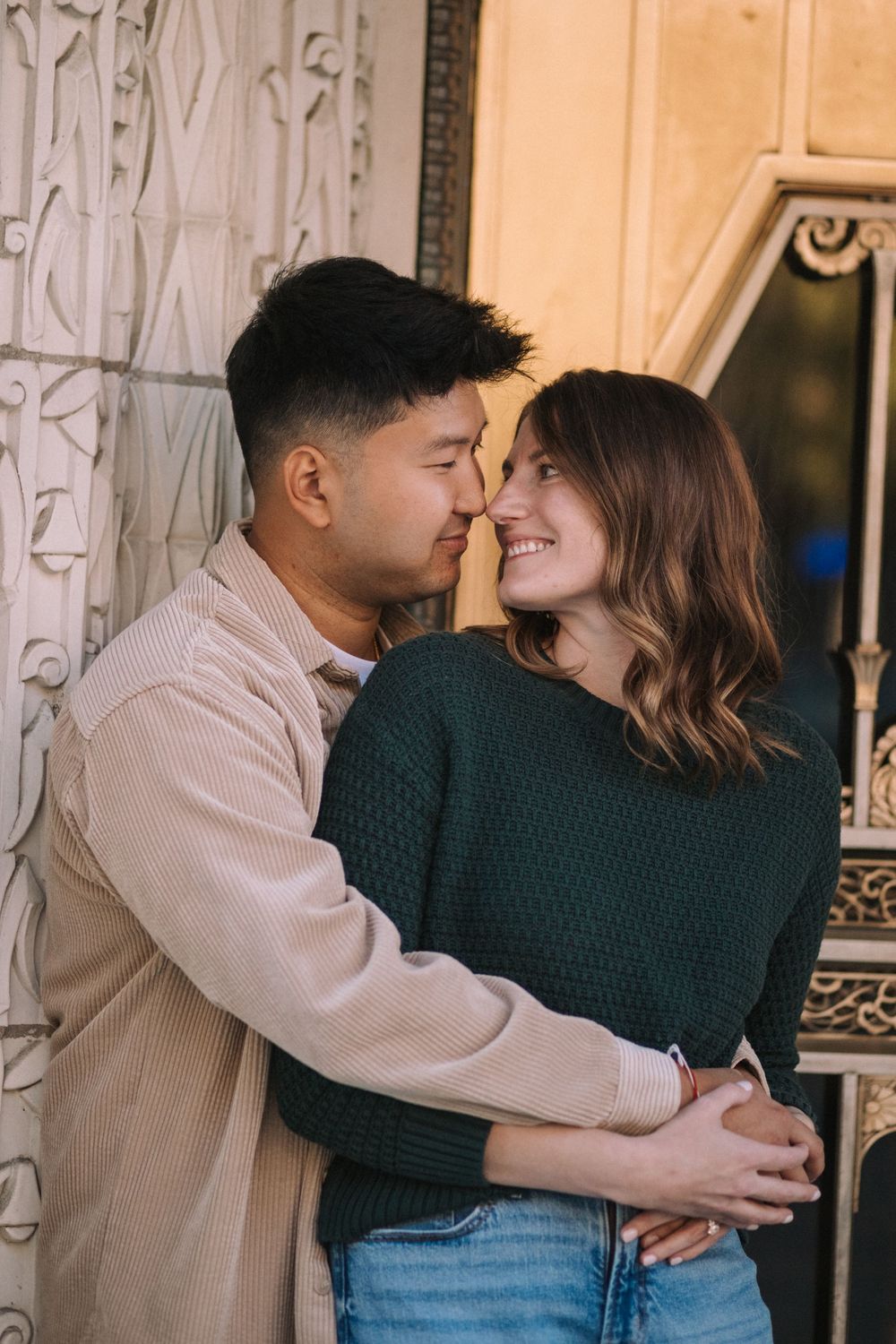 Couple in casual attire sharing intimate moment against decorative wall.