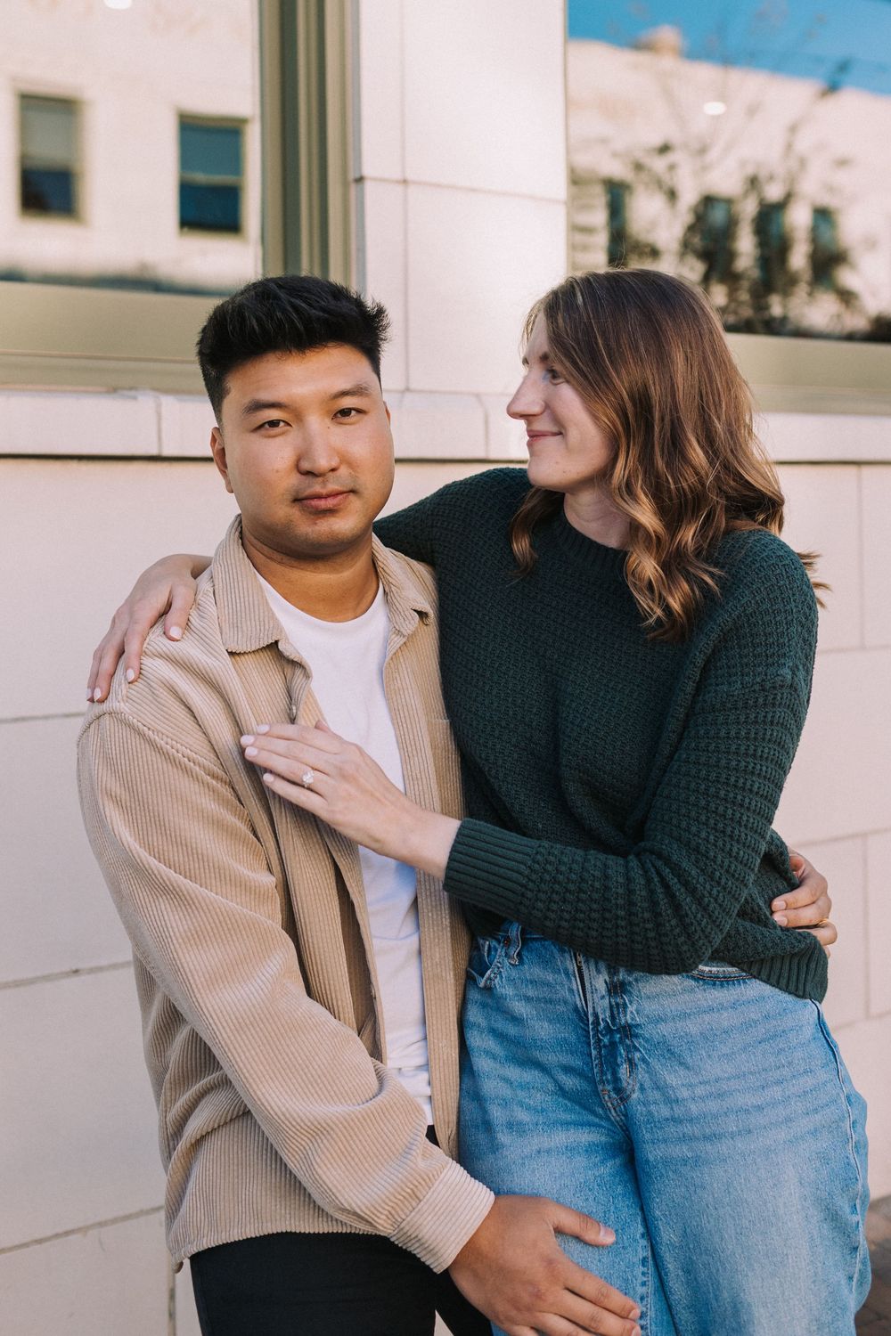 Couple in casual attire sharing intimate moments while posing against a white wall in a photo series.