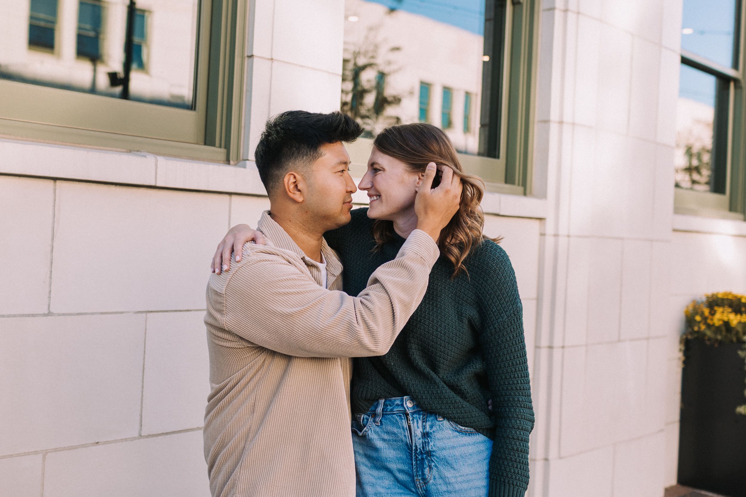 Romantic couple embracing against white building exterior wall.