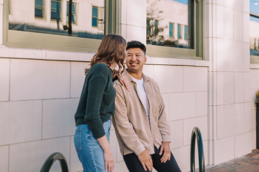 Couple laughing together against white building exterior.