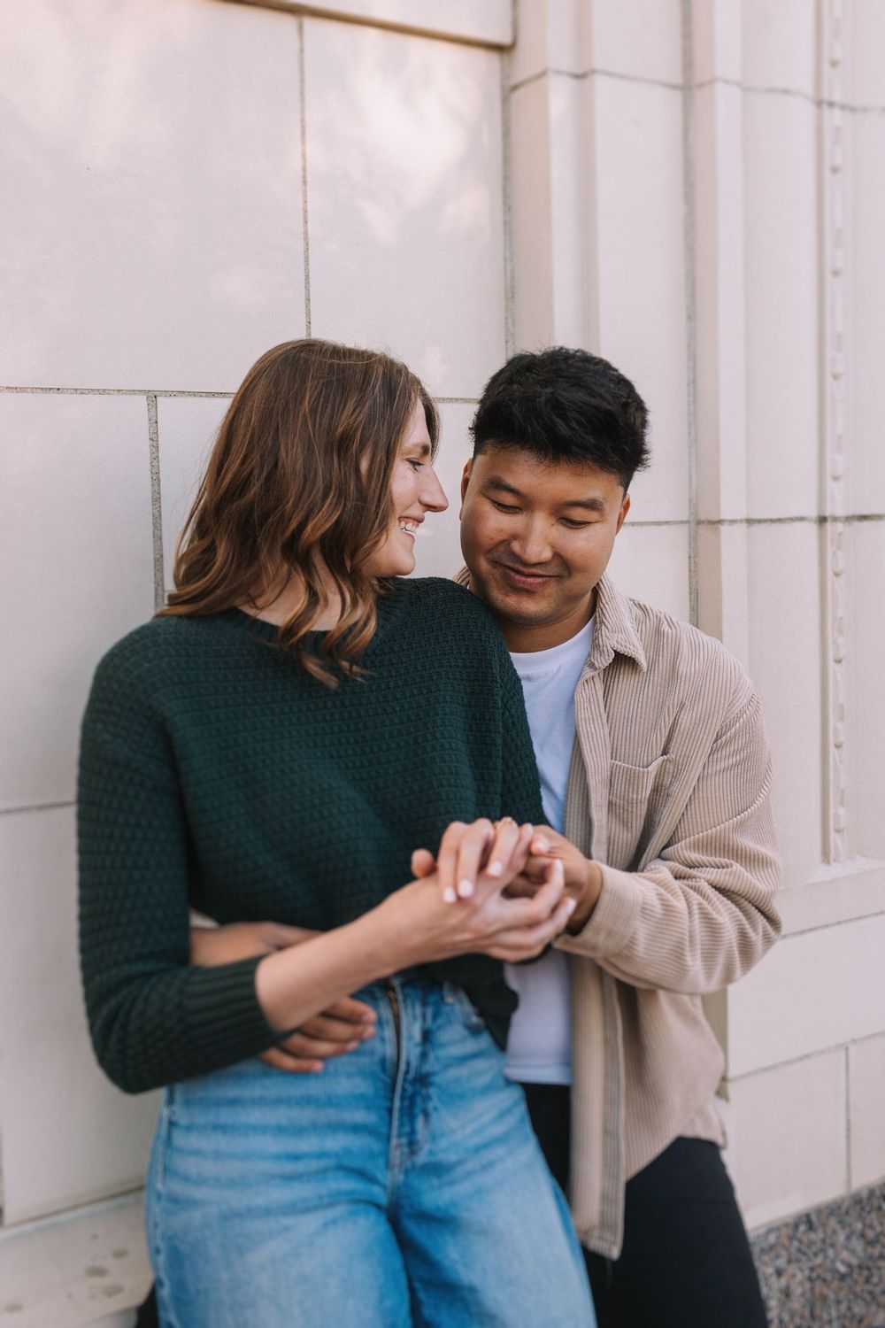 Couple holding hands and smiling against neutral wall background.