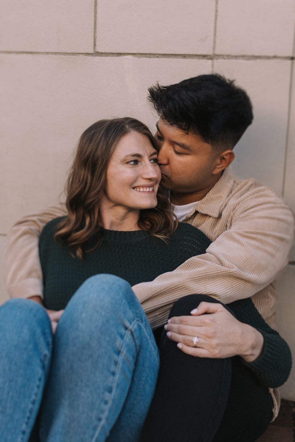 Intimate portrait of couple in casual wear against neutral wall.