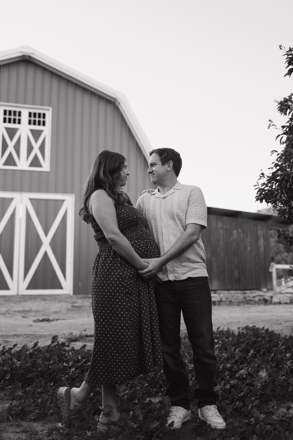 A couple poses lovingly against a rustic barn backdrop during their maternity session.