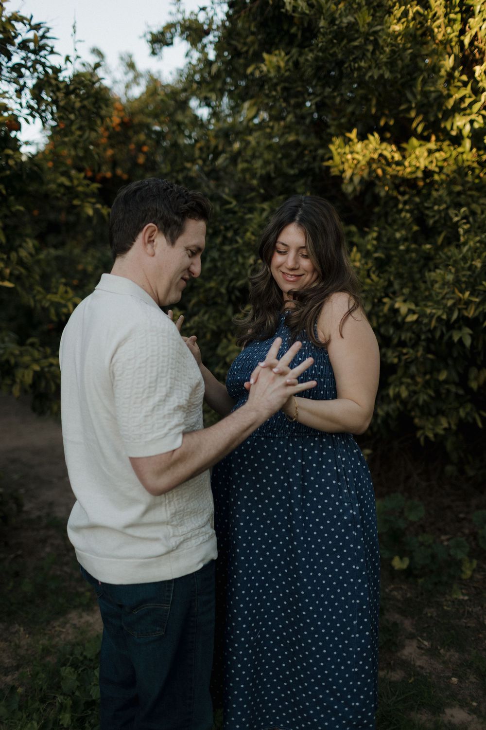 Tender moment between couple during sunset maternity photoshoot in an orchard.