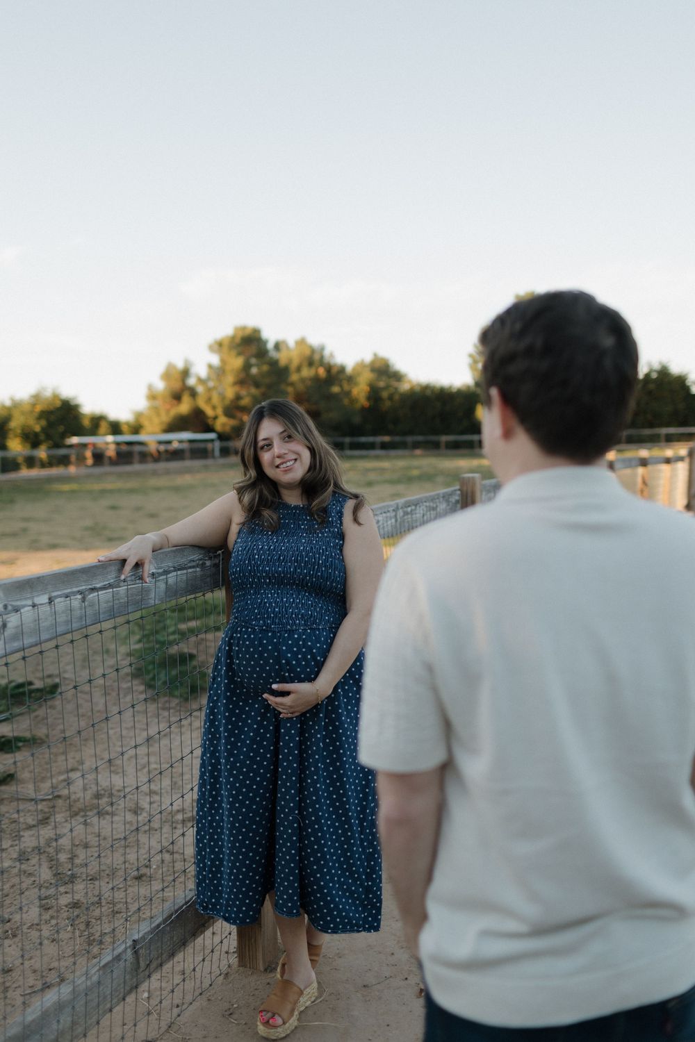 Playful maternity photos taken near a fence during golden hour.