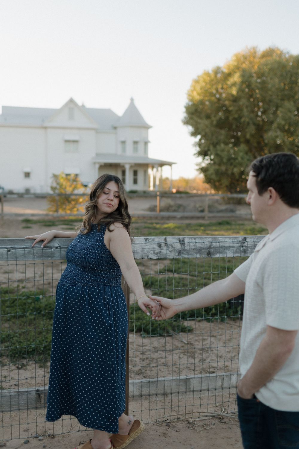 Couple shares romantic moment by wire fence with white church building in background.