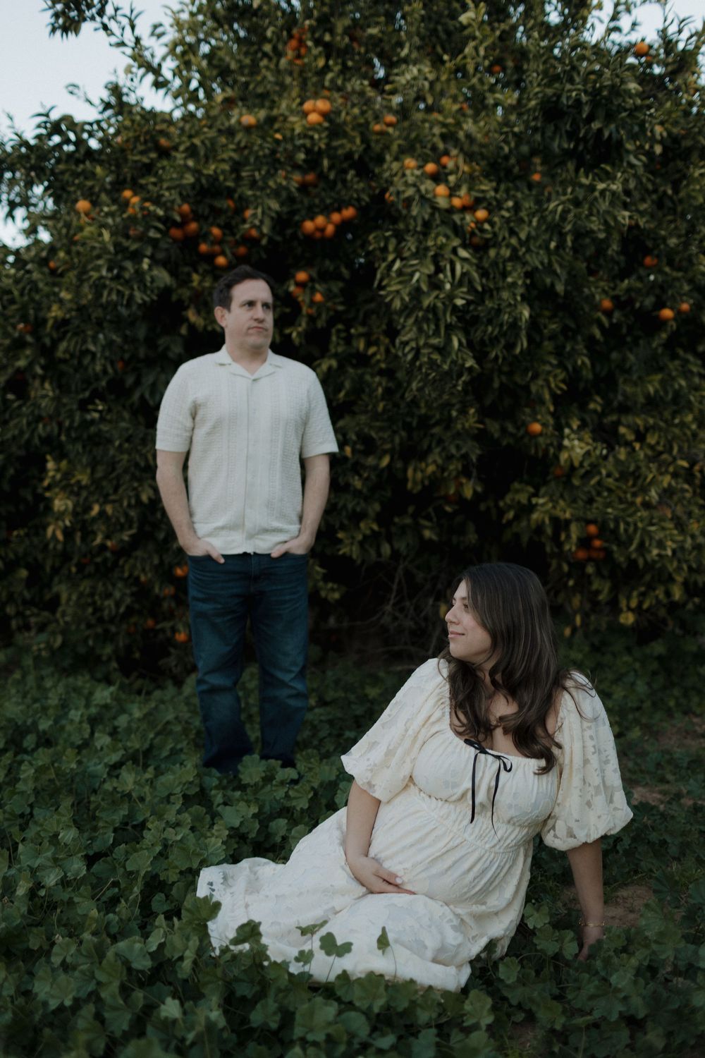 A couple poses in an orange grove with vintage-inspired styling at sunset.