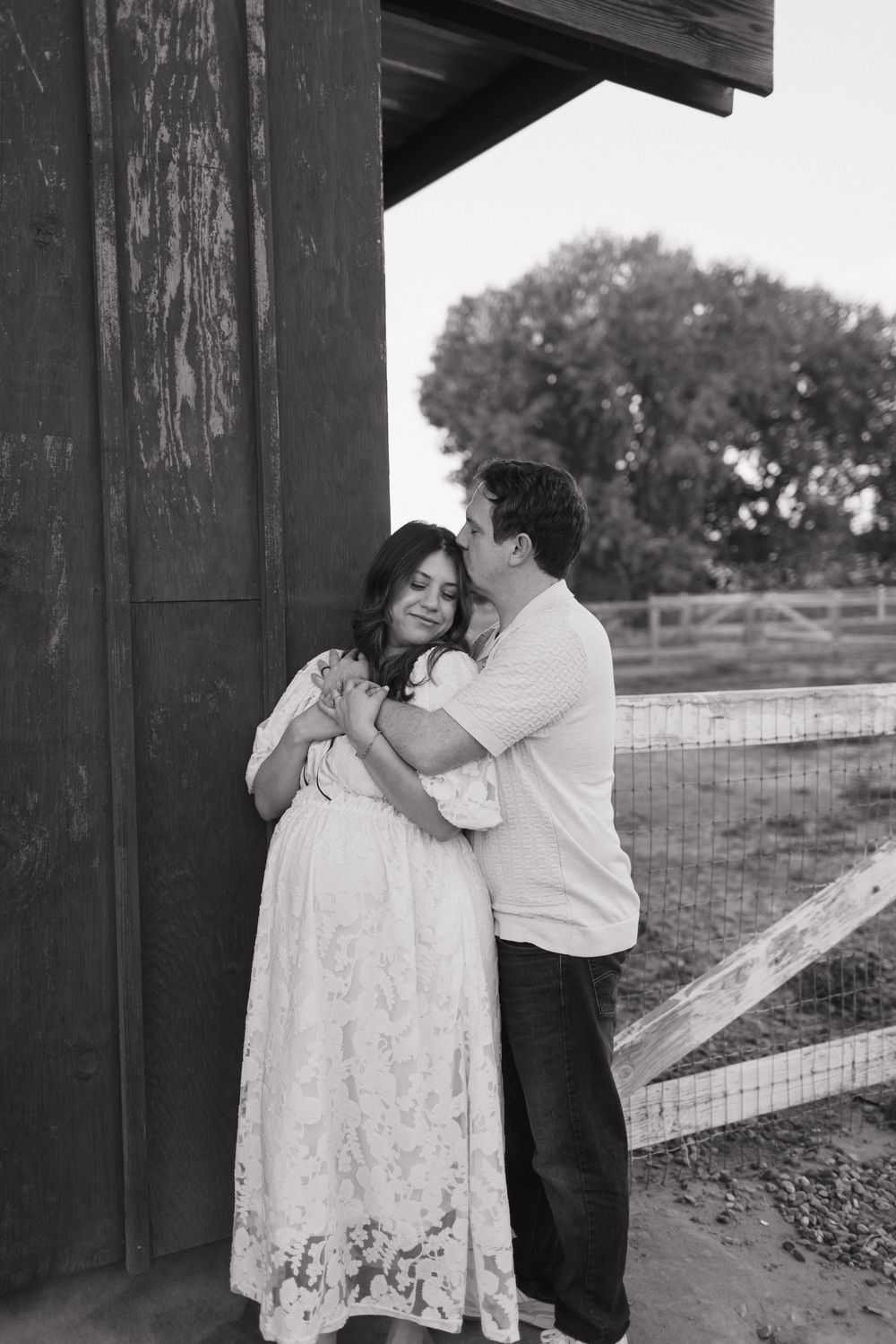 A tender black and white maternity moment captured against a rustic barn backdrop.