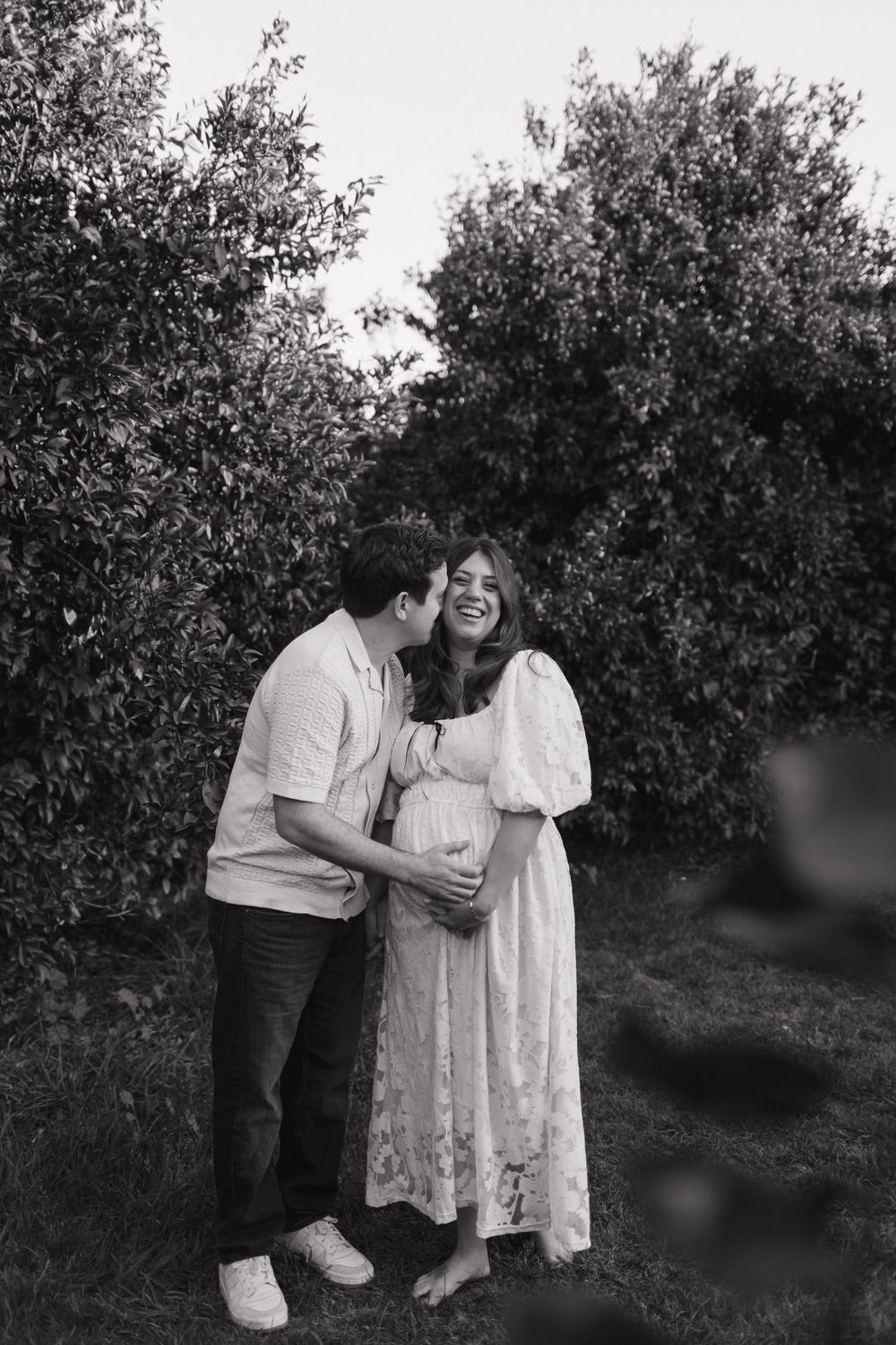 An intimate black and white maternity photo of a couple embracing among trees.