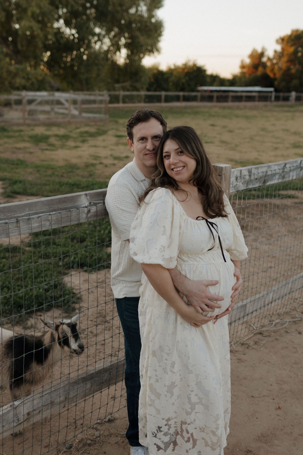 A couple poses together by a rustic farm fence during a maternity photo session.