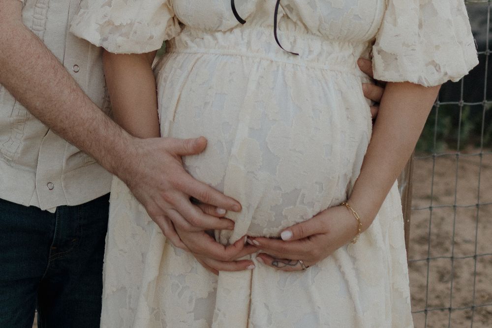 A series of romantic maternity photos showing tender moments between a couple in cream colored outfits outdoors.