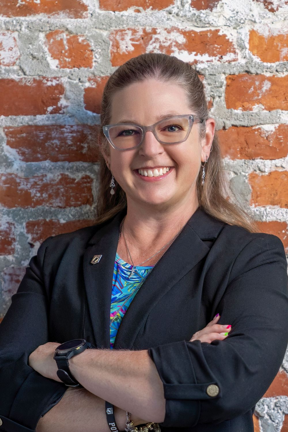 Professional headshots against a rustic brick wall showing a person in a black blazer and patterned blouse.