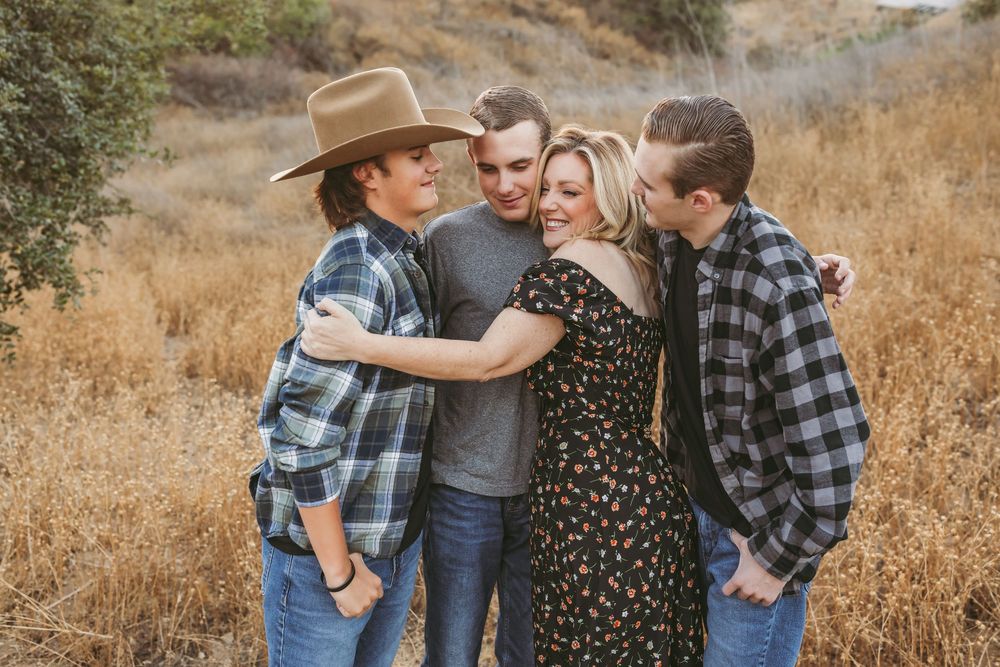 Family wearing coordinated blue and black outfits poses together in a golden field during sunset.