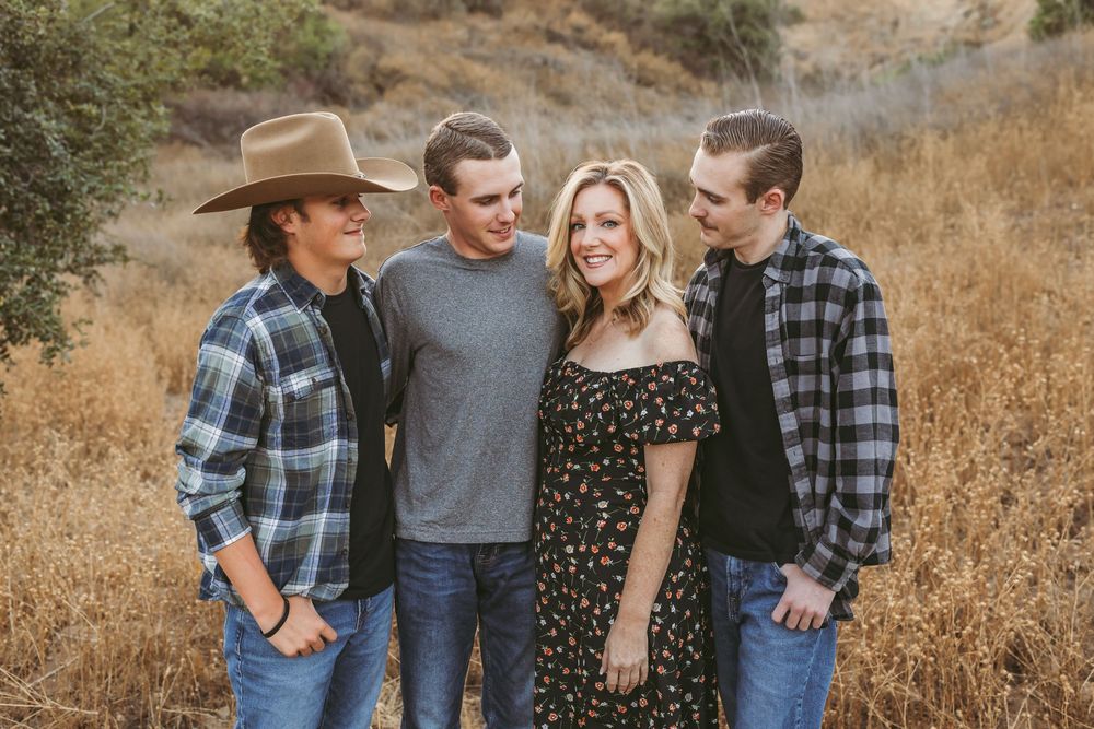 A group of friends in casual attire pose together on a golden hillside during sunset.