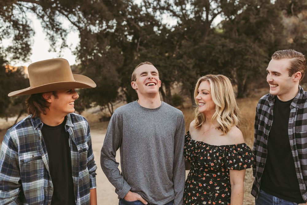 Group wearing denim and plaid gather for casual portraits under oak trees at sunset.