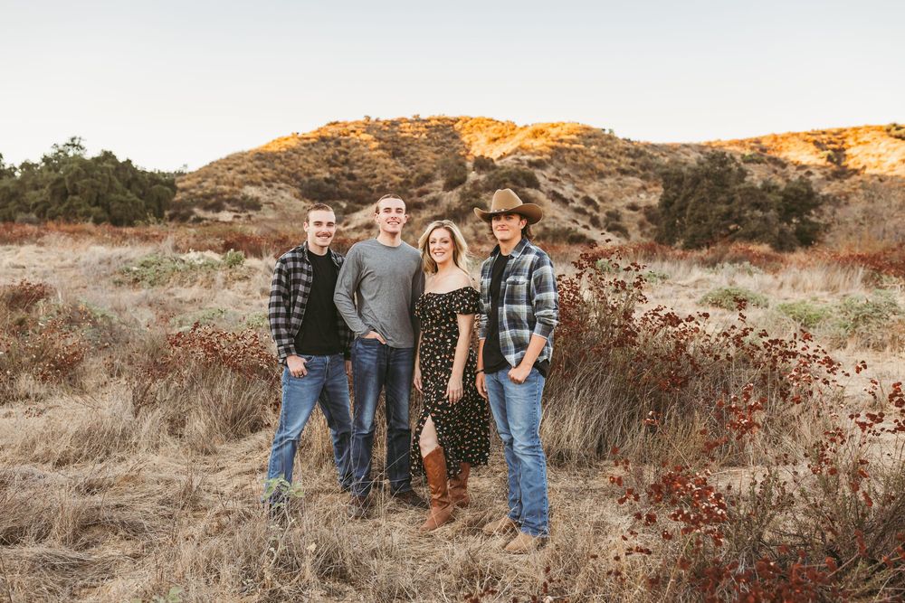 Family group poses together in a scenic outdoor setting at golden hour among autumn foliage and grasses.