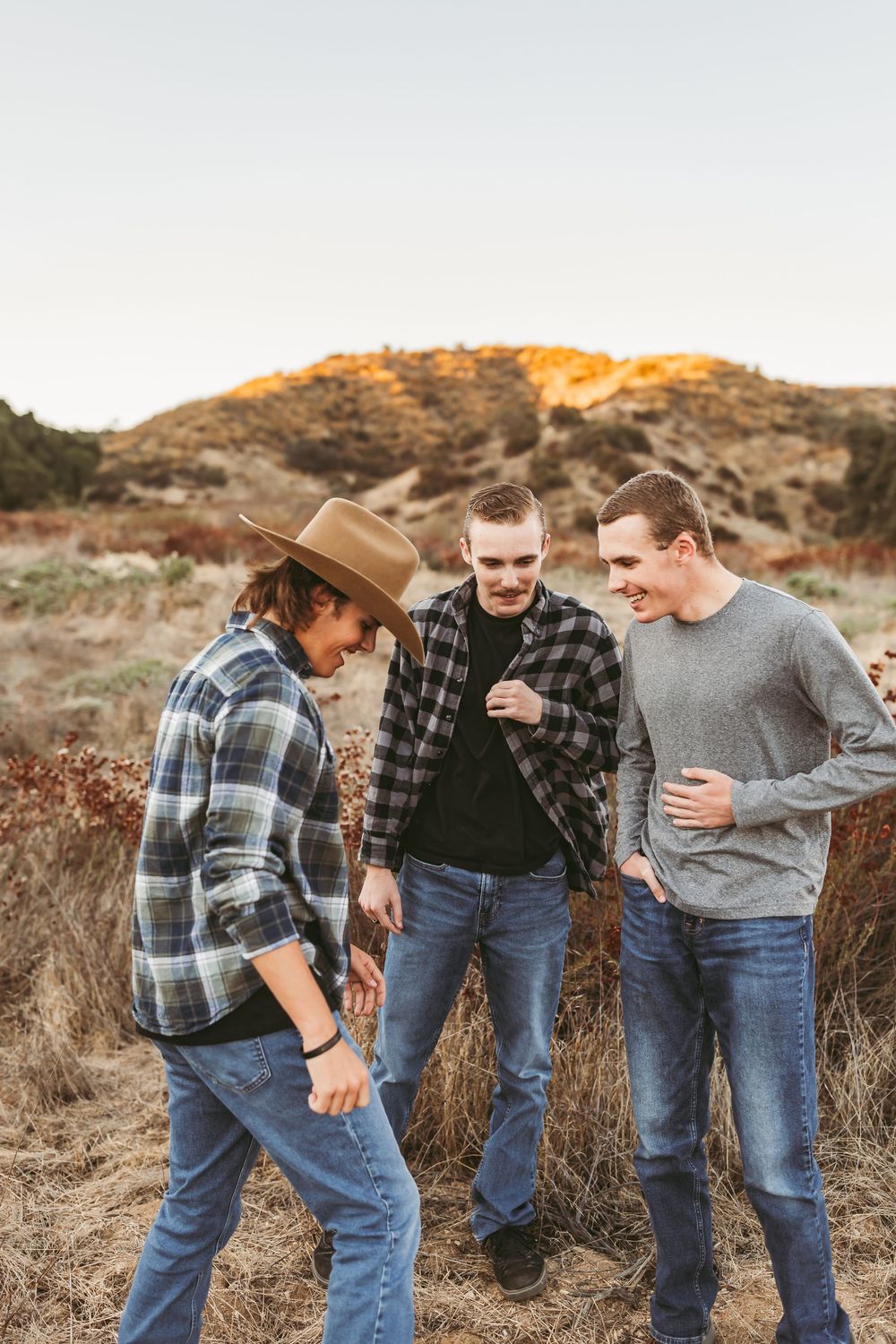 Group wearing plaid shirts and jeans laughing together in a casual outdoor setting at golden hour.