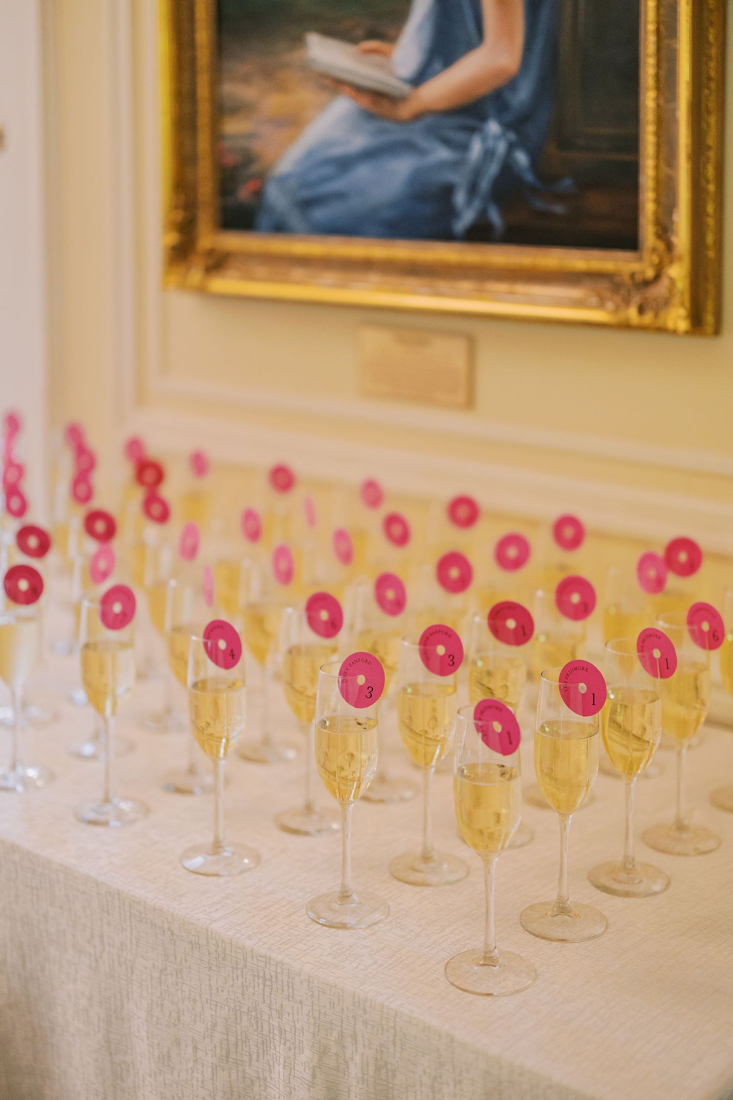Rows of champagne glasses with pink drink stirrers arranged neatly on a white tablecloth at an elegant event.