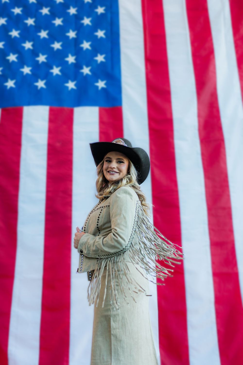 Western-themed portrait session against American flag backdrop with white fringe jacket.
