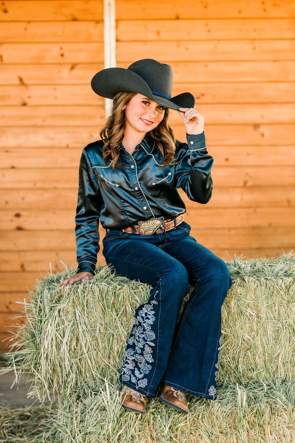 Western-style photo shoot on hay bales with denim outfit and cowboy hat.