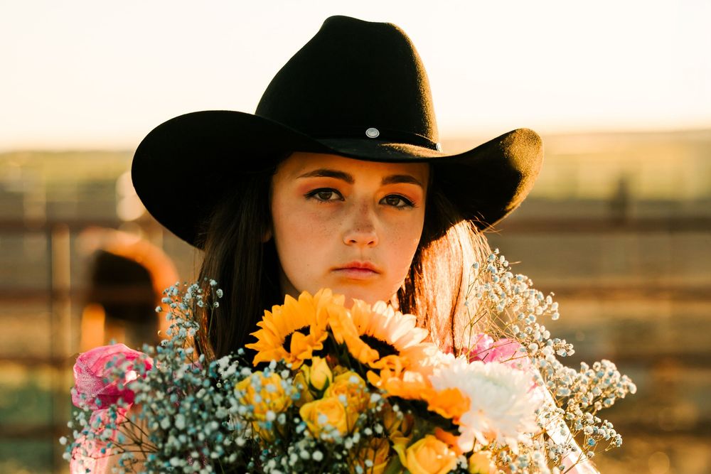 A white horse and rider pose with colorful flowers at sunset in a rustic western setting.
