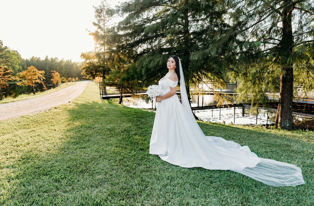 A wedding dress train trails elegantly across a sunlit grassy meadow during golden hour.