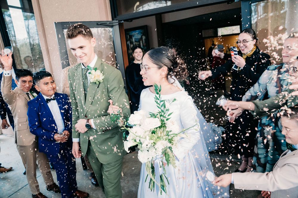 Wedding party being showered with confetti outside church entrance during celebration.