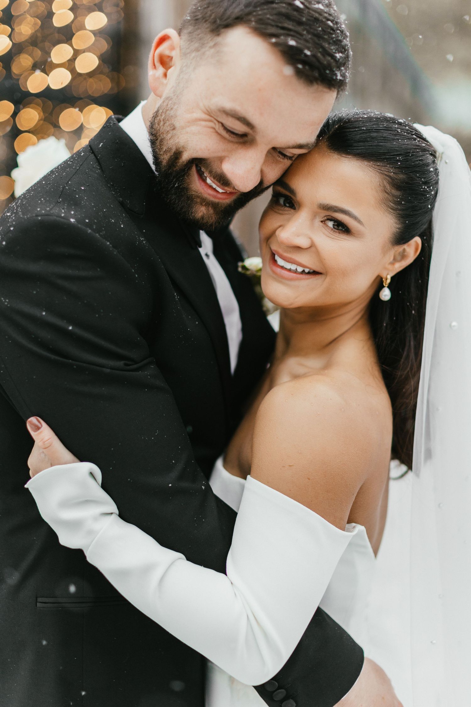 Romantic winter wedding portrait with falling snow and glowing lights.