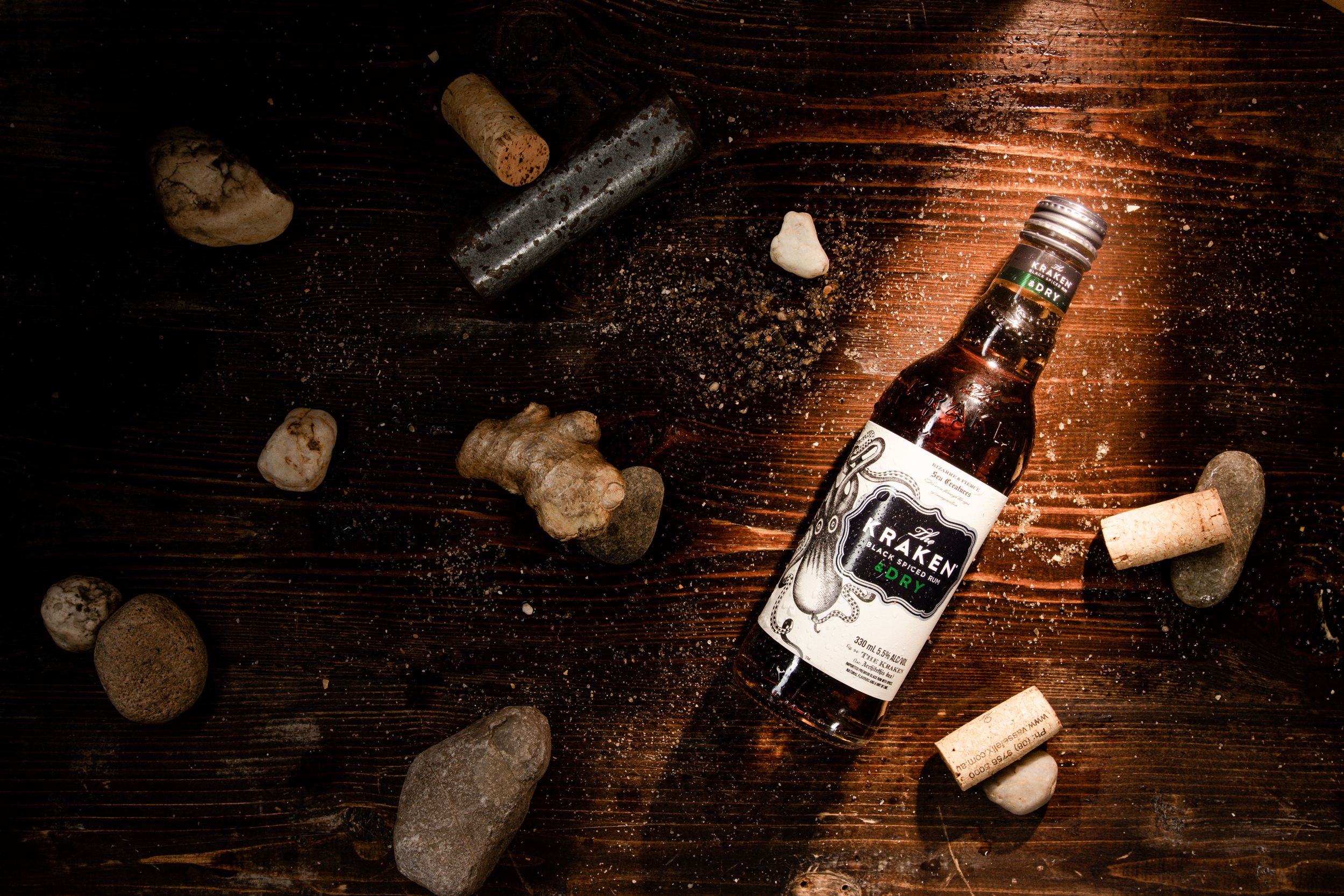 Overhead view of Kraken rum bottle surrounded by wine corks on dark wooden surface.