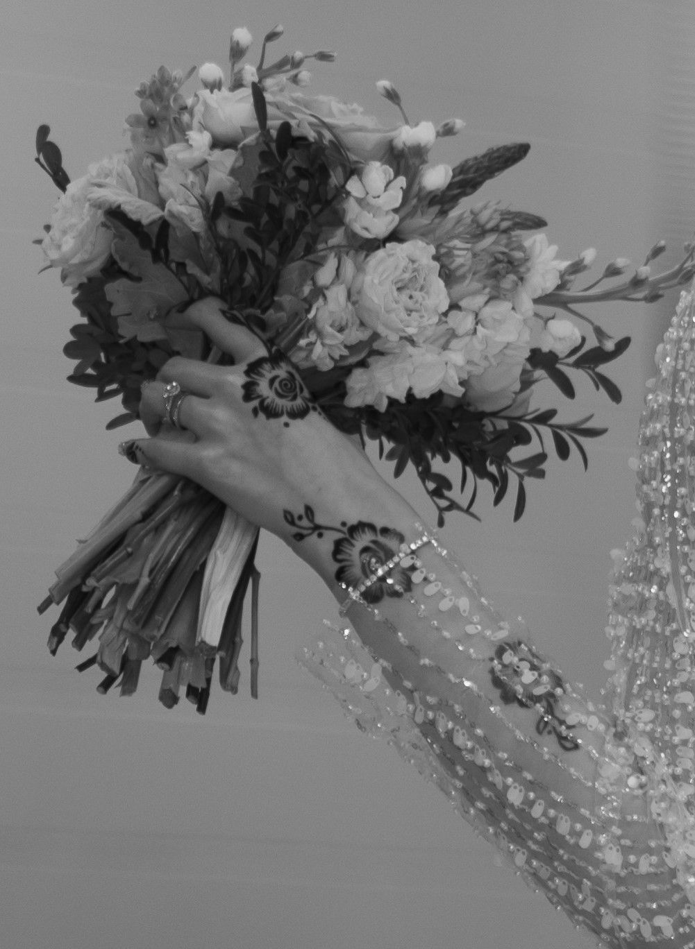 Hijabi-friendly image of a bride's hand holding a bouquet, with intricate henna designs, captured in black and white.
